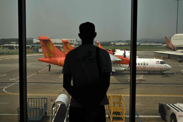 A passenger looks at Firefly aircraft parked on the tarmac at Sultan Abdul Aziz Shah Airport in Subang, Selangor state, on October 13, 2026. Malaysian low-cost carrier Firefly has extended flight cancellations between Kuala Lumpur and Singapore until October 14, the airline said, as haze from fires in neighbouring Indonesia chokes air quality across the region. (Photo by Mohd RASFAN / AFP)