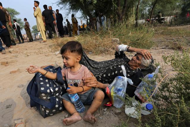 An elderly woman with a child lies on the ground next to derailed coaches of the passenger train Rehman Baba Express on the outskirts of Multan on October 13, 2026. (Photo by Shahid Saeed MIRZA / AFP)