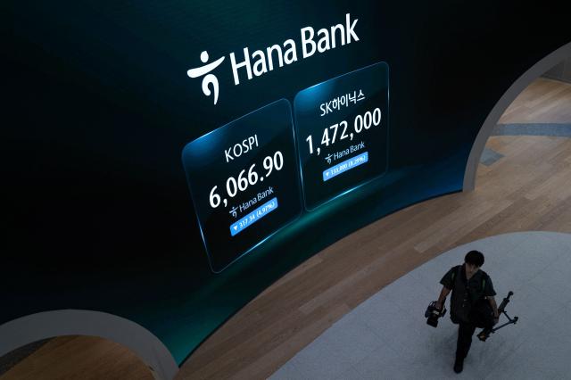 A member of the press walks past an electronic screen showing South Korea's benchmark KOSPI stock index (L) and the SK Hynix stock price (R) in a dealing room at the Hana Bank headquarters in Seoul on October 13, 2026. (Photo by Philip FONG / AFP)