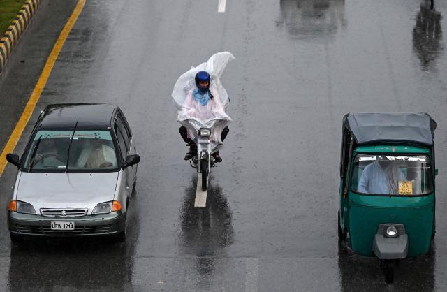 A motorcyclist covered in a polythene sheet rides along a road amid heavy rain in Peshawar on October 13, 2026. (Photo by Abdul MAJEED / AFP)