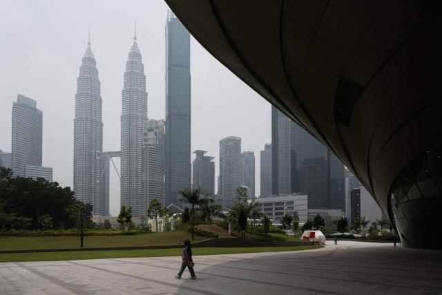 A woman walks as haze shrouds Malaysia’s Petronas Twin Towers and other commercial buildings in Kuala Lumpur on October 13, 2026. Toxic haze has shrouded parts of Indonesia, Malaysia and Singapore for weeks as Jakarta struggles to contain fires that have scorched large tracts of Borneo and Sumatra, with the smoke drifting across the region. (Photo by Mohd Rasfan / AFP)