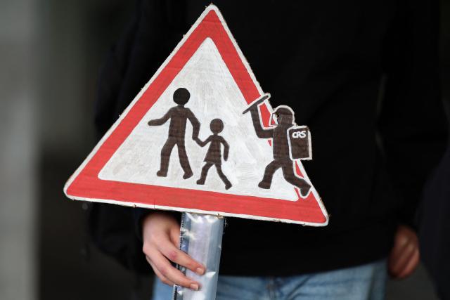 A protester holds a handmade road sign depicting a French CRS riot police officer inside a school crossing warning sign during a demonstration of high-school students in Brest, western France on October 13, 2026, as part of a nationwide high school mobilisation. France sees nationwide demonstrations on October 13 in support of students protesting poor classroom conditions for weeks, as authorities and participants remain wary of further violence. (Photo by FRED TANNEAU / AFP)