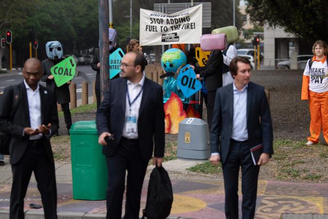 Delegates walk past Greenpeace activists protesting outside the Cape Town International Convention Centre while calling for oil and gas companies attending the African Energy Week 2026 to pay back for climate damage in Africa, in Cape Town on October 13, 2026. (Photo by RODGER BOSCH / AFP)