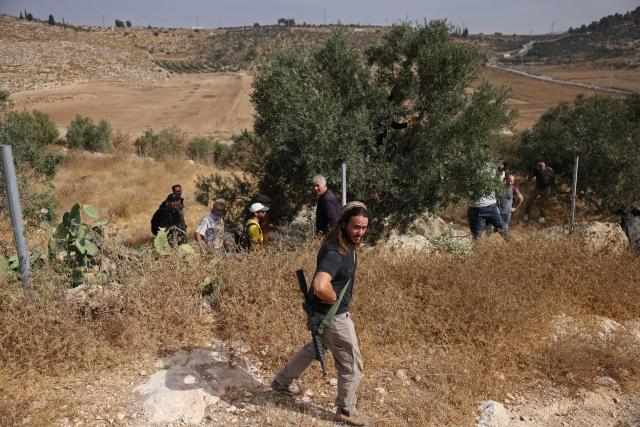 An armed Israeli settler evacuates Palestinians and Israeli activists from the area of olive tree plantation in Idna village near the occupied West Bank town of Hebron, on October 13, 2026. The olive harvest starts in the West Bank in October and makes up a large component of the agricultural economy and cultural life for most Palestinians. Extremist Israeli settlers have been seizing olive groves owned by Palestinians, who see the trees as a cultural symbol. The olive harvest is a major component of the West Banks agricultural economy, rural livelihoods and cultural life. (Photo by HAZEM BADER / AFP)