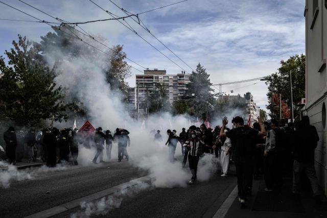 Protesters hold flags amid tear gas smoke during a demonstration of high-school students in Lyon, southeastern France on October 13, 2026, as part of a nationwide high school mobilisation. France sees nationwide demonstrations on October 13 in support of students protesting poor classroom conditions for weeks, as authorities and participants remain wary of further violence. (Photo by JEFF PACHOUD / AFP)