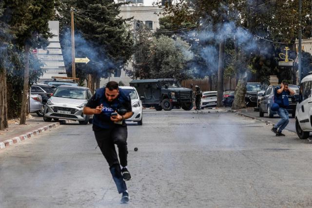 Journalists take cover from tear gas canisters fired by Israeli security forces while covering a raid in Ramallah, in the Israeli-occupied West Bank, on October 13, 2026. (Photo by Zain JAAFAR / AFP)