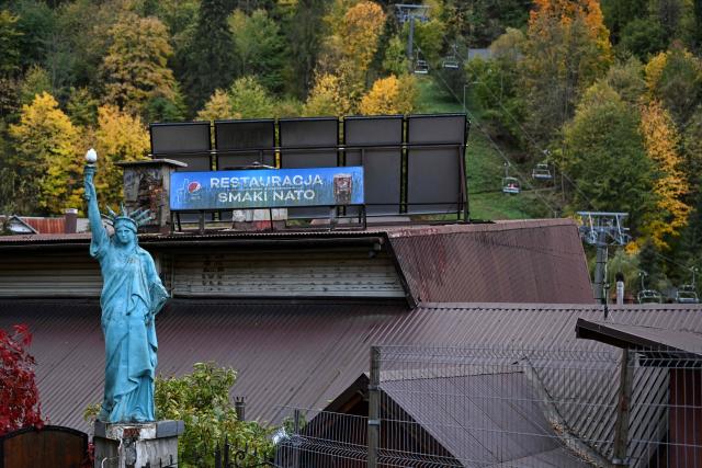 A replica of the Statue of Liberty stands on a pedestal next to the former restaurant 'Flavors of NATO', while tourists ride a ski lift in the background in Szczawnica, Lesser Poland Voivodeship on October 13, 2026. (Photo by Sergei GAPON / AFP)