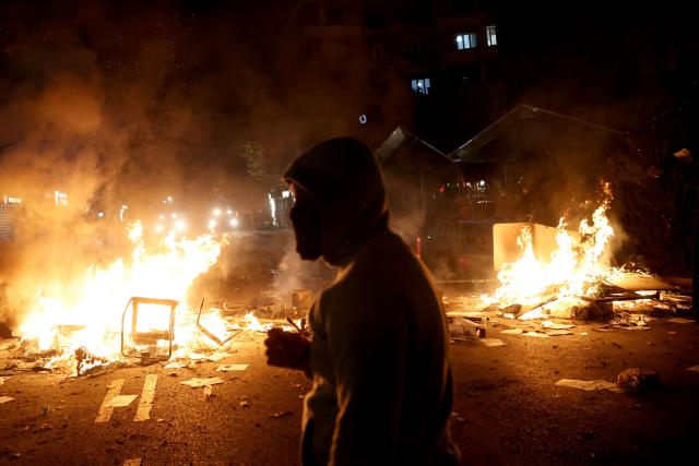 A protester stands next to a fire during clashes with riot police in Skanderbeg square during a protest in Tirana on October 13, 2026, as hundreds rallied to demand the resignation of Albanian Prime Minister Edi Rama and better education. Police used tear gas and water cannons as protesters threw stones, smashed windows at the education ministry, tore down a fence and set rubbish bins on fire, with six police officers and a female journalist injured, according to police. (Photo by Adnan Beci / AFP)