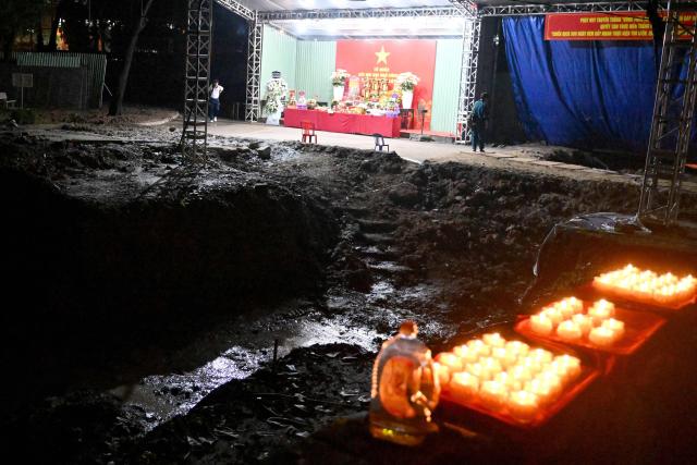 Candles are lit beside the excavation site for the remains of fallen soldiers at Le Thi Rieng Park in Ho Chi Minh City on October 13, 2026. Vietnam held funeral rites for more than 700 of its war dead on October 14, unearthed in a major push to identify those missing from decades of conflict with France and the United States. (Photo by Nhac NGUYEN / AFP)