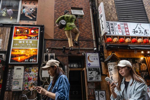 Two women walk past a bar during the lunch hour near the Shimbashi metro station in Tokyo on October 14, 2026. (Photo by Andrew CABALLERO-REYNOLDS / AFP)