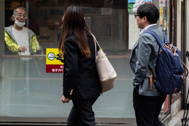A man smokes a cigarette as he watches office workers pass during lunch hour near the Shimbashi metro station in Tokyo on October 14, 2026. (Photo by Andrew CABALLERO-REYNOLDS / AFP)