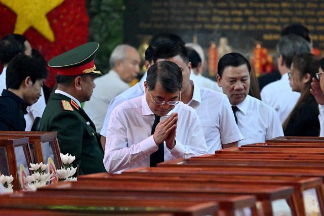 Vietnam's Prime Minister Le Minh Hung pays his respects with folded hands as he passes caskets bearing the remains of fallen soldiers at Le Thi Rieng Park in Ho Chi Minh City on October 14, 2026. Vietnam held funeral rites for more than 700 of its war dead on October 14, unearthed in a major push to identify those missing from decades of conflict with France and the United States. (Photo by Nhac NGUYEN / AFP)
