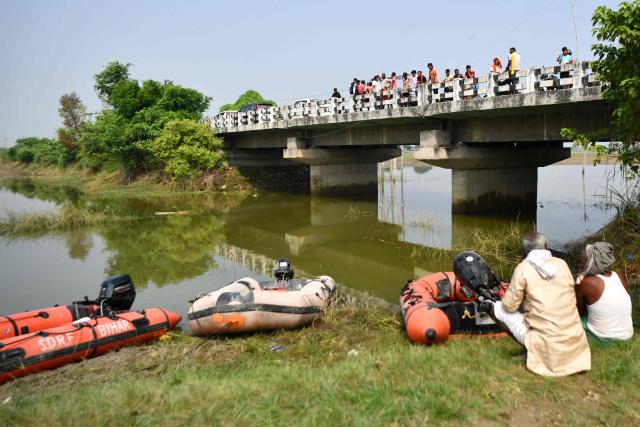 People watch from a bridge as rescue personnel conduct a search operation for the missing after a boat capsized in Ganga river in Bihar's Vaishali district on October 14, 2026. Rescuers dragged out 13 dead children from India's Ganges river after a boat capsized en route to a festival, officials said on October 14, with Prime Minister Narendra Modi expressing grief. (Photo by Sachin KUMAR / AFP)