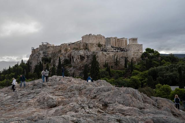 A tourist visits the Aeropagus hill as the Acropolis is seen in the background in Athens on October 14, 2026. (Photo by Angelos TZORTZINIS / AFP)