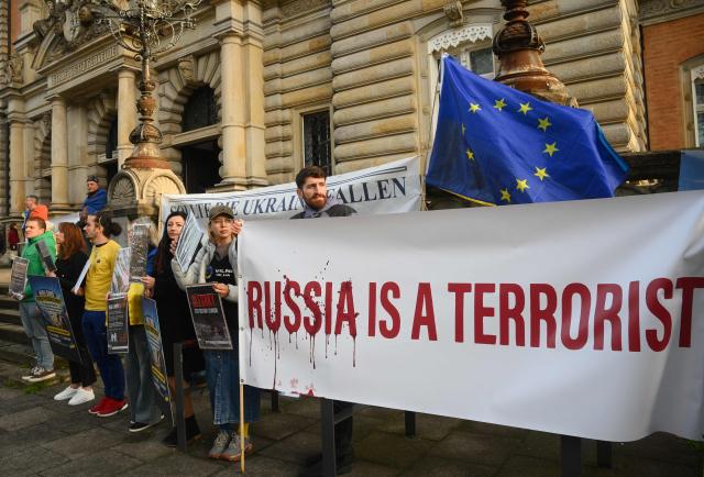 Protesters hold a banner reading "Russia is a terrorist" ahead the beginning of the trial against Ukrainian national Serhii K, a former army officer accused of the Nord Stream gas pipeline bombing around four years ago, at the Higher Regional Court in Hamburg, northern Germany on October 14, 2026. According to the indictment filed by the Federal Public Prosecutors Office, Serhii K, who was arrested last year while on vacation in Italy, is alleged to have planned the act together with other members of the Ukrainian military. In addition, the defendant is said to have led the team that blew up the natural gas pipelines under the Baltic Sea at the end of September 2022. The pipelines were used to transport Russian natural gas to Germany. According to the indictment, the attack was carried out on behalf of Ukrainian state authorities; the background was the Russian war of aggression against Ukraine, which began in early 2022. The Ukrainian government denies any official involvement. (Photo by Gregor Fischer / AFP)