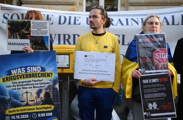 Pro-Ukraine protesters hold signs ahead the beginning of the trial against Ukrainian national Serhii K, a former army officer accused of the Nord Stream gas pipeline bombing around four years ago, at the Higher Regional Court in Hamburg, northern Germany on October 14, 2026. According to the indictment filed by the Federal Public Prosecutors Office, Serhii K, who was arrested last year while on vacation in Italy, is alleged to have planned the act together with other members of the Ukrainian military. In addition, the defendant is said to have led the team that blew up the natural gas pipelines under the Baltic Sea at the end of September 2022. The pipelines were used to transport Russian natural gas to Germany. According to the indictment, the attack was carried out on behalf of Ukrainian state authorities; the background was the Russian war of aggression against Ukraine, which began in early 2022. The Ukrainian government denies any official involvement. (Photo by Gregor Fischer / AFP)