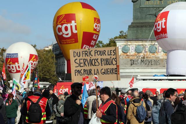 A protester holds a placard reading "Money for public services, not for war" as people gather at Place de la Bastille ahead of a march to the headquarters of supplementary pension scheme Agirc-Arrco, called by the CGT trade union to demand pensions be indexed to inflation after the 2026 freeze, in Paris, on October 14, 2026. (Photo by MEHDI FEDOUACH / AFP)