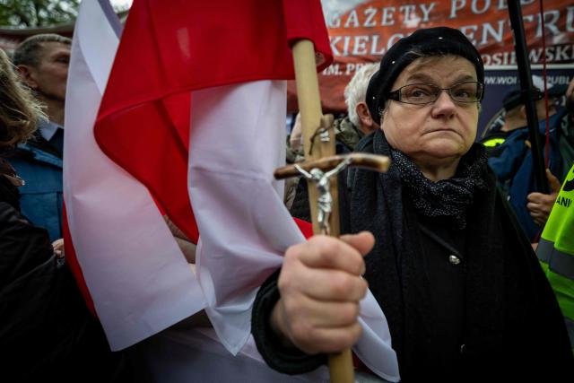 A woman holds a crucifix and the polish national flag as anti-government protestors attend a demonstration in front of the Constitutional Court, Poland's highest court, in Warsaw on October 14, 2026. Right-wing protestors clashed with police in front of Poland's highest court on October 14, attempting to block its judges from entering the building and defending its overhaul by the previous government. (Photo by Wojtek RADWANSKI / AFP)