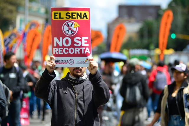 A demonstrator holds a placard reading "SENA Must Not Be Cut" during a protest against the government of Colombian President Abelardo de la Espriella in Bogota on October 14, 2026, as part of a nationwide day of demonstrations called by labor unions, teachers' organizations, student groups and opposition sectors. (Photo by Sebastian BARROS / AFP)