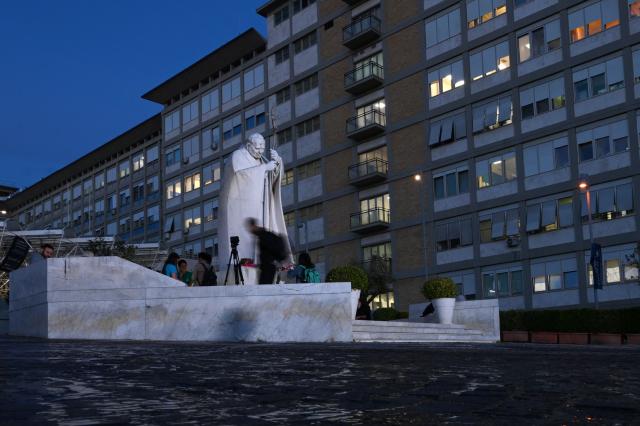 People pray at the statue of John Paul II outside the Gemelli University Hospital, where Pope Leo XIV is recovering after undergoing surgery to remove a cancerous tumour from his right lung, in Rome on October 14, 2026.  (Photo by Tiziana FABI / AFP)
