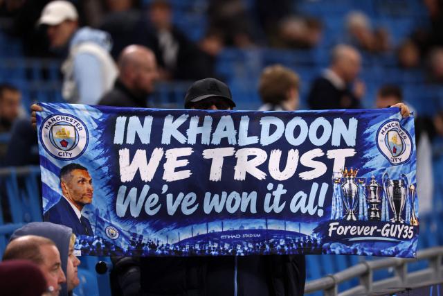 A City fan displays a flag with a slogan in support of Manchester City's Emirati chairman Khaldoon al-Mubarak ahead of the UEFA Champions League, league phase football match between Manchester City and Paris Saint Germain at the Etihad Stadium in Manchester, north west England, on October 14, 2026. (Photo by FRANCK FIFE / AFP)
