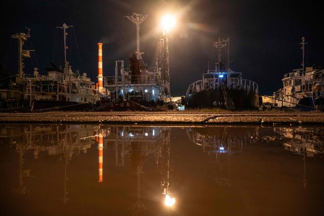A flare stack is reflected near boats as it burns off byproduct gasses at the Toa oil refinery in Kawasaki on October 14, 2026. (Photo by Andrew Caballero-Reynolds / AFP)