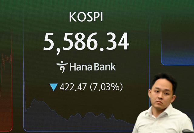 A currency dealer walks past an electronic screen showing South Korea's benchmark stock index (KOSPI) in a foreign exchange dealing room at the Hana Bank headquarters in Seoul on October 15, 2026. Japan's benchmark stock index lost more than three percent on October 15, and South Korean shares shed six percent, after Wall Street ended lower following a hotter-than-expected US inflation reading. (Photo by Jung Yeon-je / AFP)