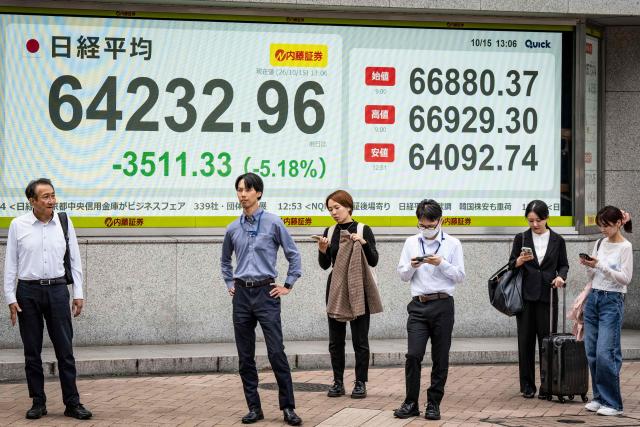 People wait to cross a street in front of an electronic quotation board displaying the Nikkei Stock Average on the Tokyo Stock Exchange in Tokyo on October 15, 2026. (Photo by Yuichi YAMAZAKI / AFP)