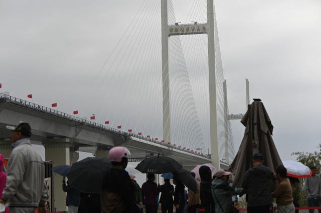 People gather near the new cross-border bridge linking China and North Korea in Dandong, Liaoning Province, on October 15, 2026. A new four-lane road bridge linking China and North Korea finally opened on October 15, 12 years late, enabling the Asian giant and its isolated nuclear-armed neighbour to step up cross-border trade substantially. (Photo by Michael ZHANG / AFP)