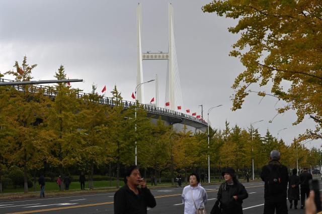 People gather near the new cross-border bridge linking China and North Korea in Dandong, Liaoning Province, on October 15, 2026. A new four-lane road bridge linking China and North Korea finally opened on October 15, 12 years late, enabling the Asian giant and its isolated nuclear-armed neighbour to step up cross-border trade substantially. (Photo by Michael ZHANG / AFP)