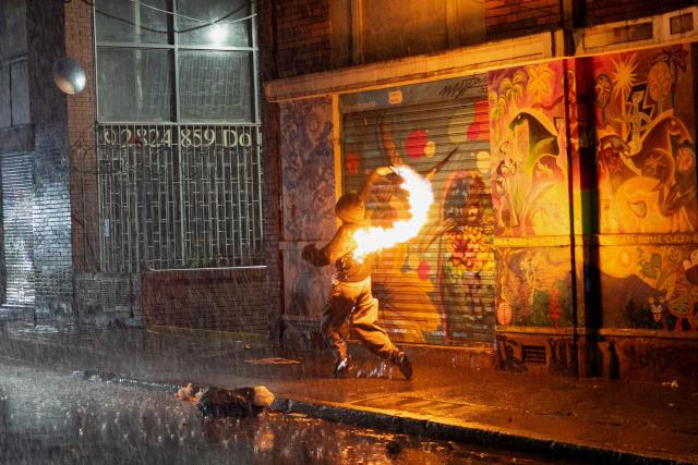 A demonstrator throws a Molotov cocktail during clashes with police following a protest against Colombia's President Abelardo de la Espriella in Bogota on October 14, 2026. Thousands of Colombians took to the streets of cities across the country on October 14, 2026, to protest the policies of new right-wing President Abelardo de la Espriella. (Photo by Pierre BRIOULT / AFP)
