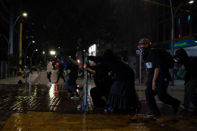 Demonstrators take cover from a police water cannon during clashes following a protest against Colombian President Abelardo de la Espriella in Bogotá, Colombia, on October 14, 2026. Thousands of Colombians took to the streets of cities across the country on October 14, 2026, to protest the policies of new right-wing President Abelardo de la Espriella. (Photo by Pierre BRIOULT / AFP)
