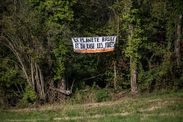 This photograph shows a banner reading "The planet is burning, and we’re cutting down forests" against the controversial construction of the A412 motorway, near Perrignier, Haute-Savoie, France, on October 14, 2026. A coalition of associations, farmers, and residents on October 14, 2026, sought to halt construction of the A412 motorway, arguing that its environmental impact runs “counter to the climate emergency.” While a court ruling is expected on October 15, 2026, protesters have staged near-daily demonstrations, resulting in dozens of detentions and fines, according to organizers. (Photo by Fabrice COFFRINI / AFP)