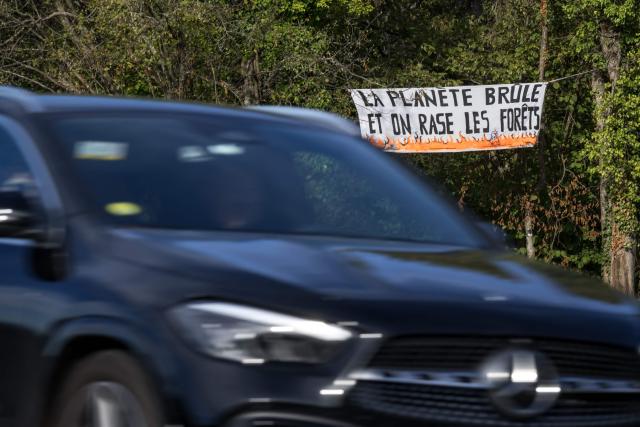 This photograph shows a banner reading "The planet is burning, and we’re cutting down forests" against the controversial construction of the A412 motorway, near Perrignier, Haute-Savoie, France, on October 14, 2026. A coalition of associations, farmers, and residents on October 14, 2026, sought to halt construction of the A412 motorway, arguing that its environmental impact runs “counter to the climate emergency.” While a court ruling is expected on October 15, 2026, protesters have staged near-daily demonstrations, resulting in dozens of detentions and fines, according to organizers. (Photo by Fabrice COFFRINI / AFP)