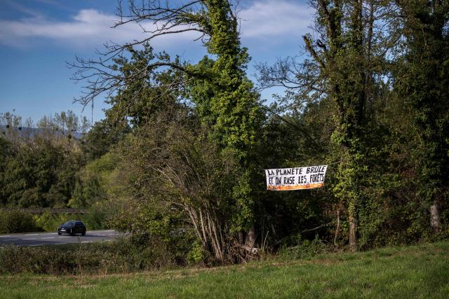 This photograph shows a banner reading "The planet is burning, and we’re cutting down forests" against the controversial construction of the A412 motorway, near Perrignier, Haute-Savoie, France, on October 14, 2026. A coalition of associations, farmers, and residents on October 14, 2026, sought to halt construction of the A412 motorway, arguing that its environmental impact runs “counter to the climate emergency.” While a court ruling is expected on October 15, 2026, protesters have staged near-daily demonstrations, resulting in dozens of detentions and fines, according to organizers. (Photo by Fabrice COFFRINI / AFP)