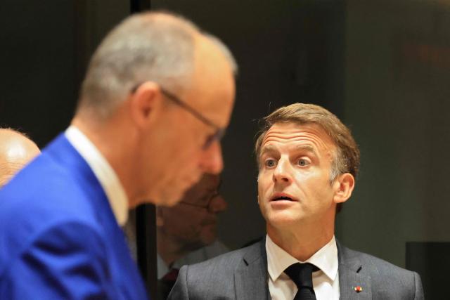 France's President Emmanuel Macron (R) stands as Germany's Chancellor Friedrich Merz walks by ahead of a round table as part of a European Union summit at the EU headquarters in Brussels on October 15, 2026. EU leaders head on October 15, 2026 for their biggest clash yet over the bloc's next long-term budget, as they race to lock in a deal before next year's French presidential election. (Photo by Ludovic MARIN / AFP)