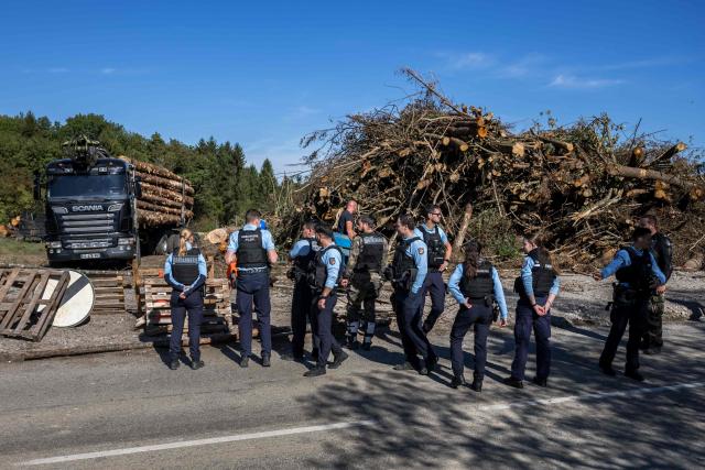 Police officers stand along a road following an intervention after protesters blocked a truck carrying logs during the controversial construction of the A412 motorway, near Perrignier, Haute-Savoie, France, on October 14, 2026. A coalition of associations, farmers, and residents on October 14, 2026, sought to halt construction of the A412 motorway, arguing that its environmental impact runs “counter to the climate emergency.” While a court ruling is expected on October 15, 2026, protesters have staged near-daily demonstrations, resulting in dozens of detentions and fines, according to organizers. (Photo by Fabrice COFFRINI / AFP)