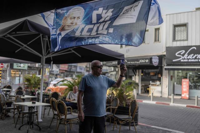 An Israeli man makes a video call beneath a campaign banner of Israeli Prime Minister Benjamin Netanyahu's Likud party in Ashkelon on October 15, 2026. Israel heads to the polls on October 27 in its first election since the October 7, 2023 Hamas-led attack, in what is seen as a referendum on the prime minister. (Photo by Ilia YEFIMOVICH / AFP)