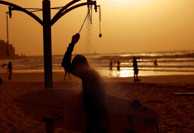 An Israeli surfer showers after existing the sea at sunset along the shores of the coastal city of Tel Aviv, on October 15, 2026. (Photo by JACK GUEZ / AFP)