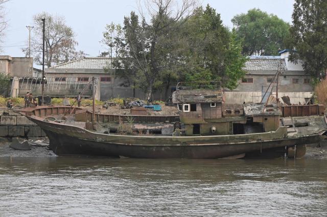 North Korean men are seen near an old boat on the waterfront of the Yalu River in the North Korean town of Sinuiju, viewed from the border city of Dandong, in China's northeast Liaoning province, on October 15, 2026.  (Photo by Michael ZHANG / AFP)