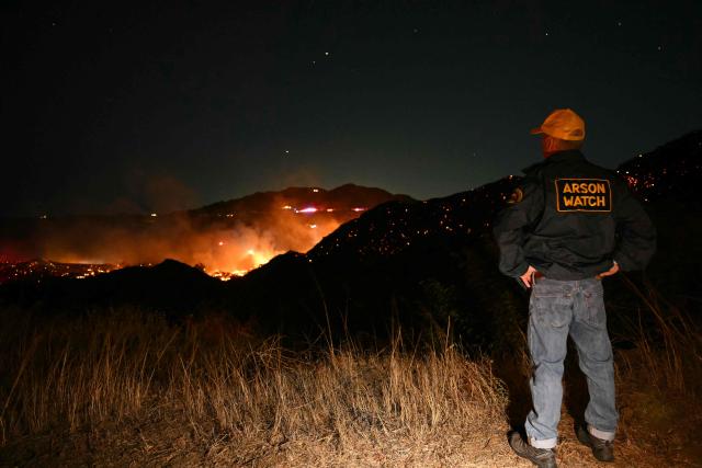 An Arson Watch volunteer looks at the Bryson Fire burning in Malibu, California on October 15, 2026. The brush fire in the mountains west of Los Angeles prompted evacuation warnings from officials, as powerful Santa Ana winds risked spreading the blaze rapidly. (Photo by Patrick T. Fallon / AFP)