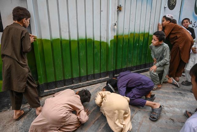 Children try to peek through the sealed entrance of school a day after its roof collapsed killing several students in Peshawar on October 16, 2026. The roof of a school collapsed in Pakistan's northwestern city of Peshawar on October 16, killing 32 students mostly younger than 14, and a teacher, officials said, blaming the accident on dilapidated infrastructure. (Photo by Abdul MAJEED / AFP)