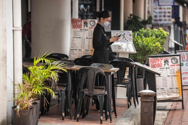 A bar employee wearing a face mask looks at a smartphone as she waits for customers outside a bar in Singapore on October 16, 2026, as the country continues to be shrouded in haze caused by fires in Indonesia. Toxic haze has covered parts of Indonesia, Malaysia and Singapore for weeks as Jakarta struggles to contain fires that have scorched large tracts of Borneo and Sumatra, with the smoke drifting across the region. (Photo by Yuichi YAMAZAKI / AFP)