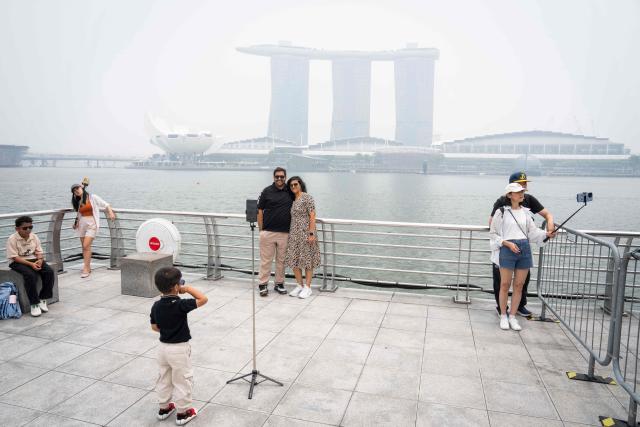 Tourists take photographs in front of the Marina Bay Sands in Singapore on October 16, 2026, as the country continues to be shrouded in haze caused by fires in Indonesia. Toxic haze has covered parts of Indonesia, Malaysia and Singapore for weeks as Jakarta struggles to contain fires that have scorched large tracts of Borneo and Sumatra, with the smoke drifting across the region. (Photo by Yuichi YAMAZAKI / AFP)