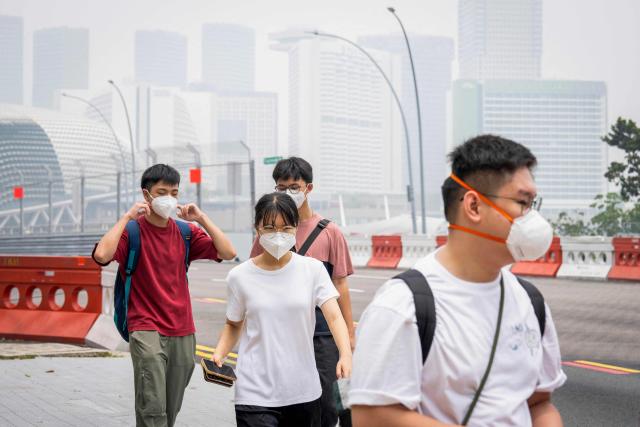 People wearing face masks walk along a street in Singapore on October 16, 2026, as the country continues to be shrouded in haze caused by fires in Indonesia. Toxic haze has covered parts of Indonesia, Malaysia and Singapore for weeks as Jakarta struggles to contain fires that have scorched large tracts of Borneo and Sumatra, with the smoke drifting across the region. (Photo by Yuichi YAMAZAKI / AFP)