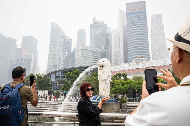 Tourists take photographs in front of the Merlion in Singapore on October 16, 2026, as the country continues to be shrouded in haze caused by fires in Indonesia. Toxic haze has covered parts of Indonesia, Malaysia and Singapore for weeks as Jakarta struggles to contain fires that have scorched large tracts of Borneo and Sumatra, with the smoke drifting across the region. (Photo by Yuichi YAMAZAKI / AFP)