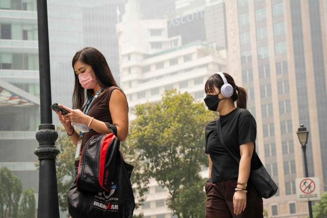 People wearing face masks walk through the business district in Singapore on October 16, 2026, as the country continues to be shrouded in haze caused by fires in Indonesia. Toxic haze has covered parts of Indonesia, Malaysia and Singapore for weeks as Jakarta struggles to contain fires that have scorched large tracts of Borneo and Sumatra, with the smoke drifting across the region. (Photo by Yuichi YAMAZAKI / AFP)