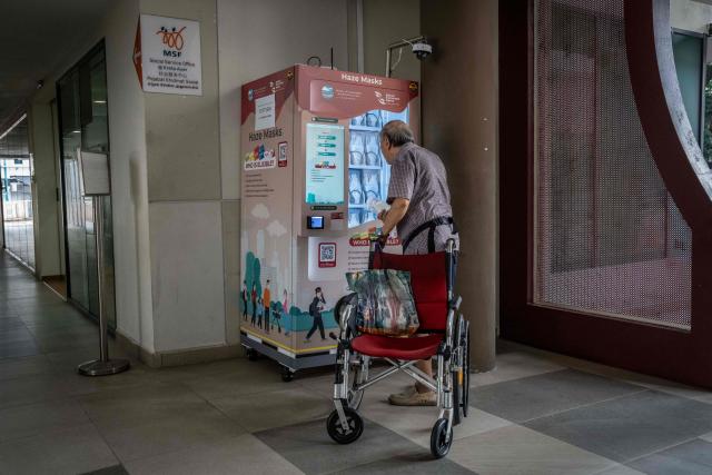 An elderly man collects an N95 face mask from a vending machine in Singapore on October 16, 2026, as the country continues to be shrouded in haze caused by fires in Indonesia. Toxic haze has covered parts of Indonesia, Malaysia and Singapore for weeks as Jakarta struggles to contain fires that have scorched large tracts of Borneo and Sumatra, with the smoke drifting across the region. (Photo by Yuichi YAMAZAKI / AFP)