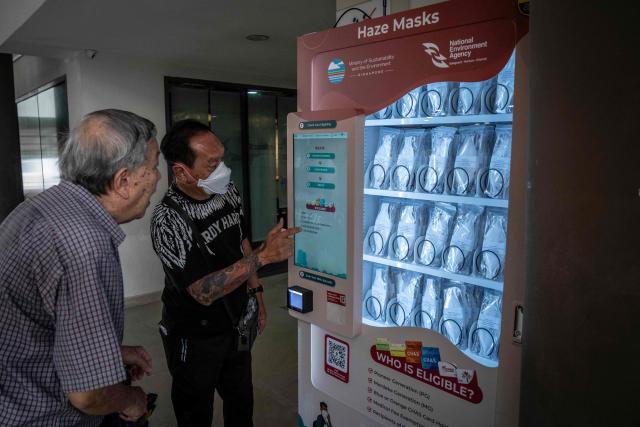 A man (R) helps an elderly man use an N95 face mask vending machine in Singapore on October 16, 2026, as the country continues to be shrouded in haze caused by fires in Indonesia. Toxic haze has covered parts of Indonesia, Malaysia and Singapore for weeks as Jakarta struggles to contain fires that have scorched large tracts of Borneo and Sumatra, with the smoke drifting across the region. (Photo by Yuichi YAMAZAKI / AFP)