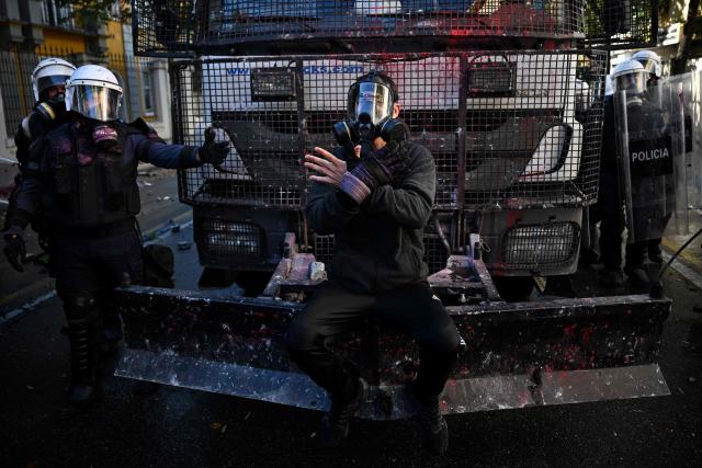 A protester gestures as he sits on the bumper of a police vehicle during an anti-government demonstration in central Tirana on October 16, 2026, as protests continued for a fourth consecutive day over university conditions and demands for the resignation of Albanian Prime Minister Edi Rama. For more than four months, anti-government protests in Albanian have routinely drawn crowds in their thousands. They were originally sparked by a luxury hotel project linked to US President Donald Trump's family, which scientists said in July 2026 had already caused irreparable damage to a once pristine stretch of Albania's coast. (Photo by Armend NIMANI / AFP)